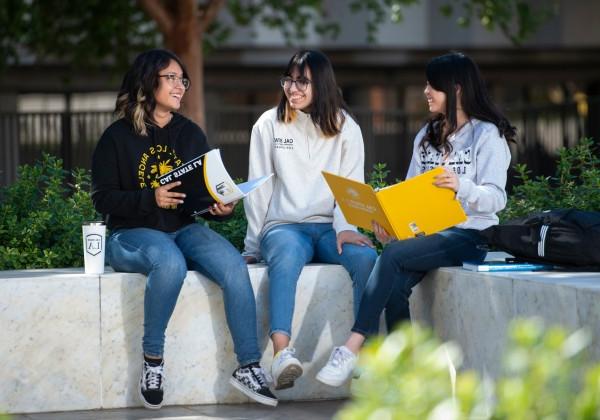 3 students sitting on a bench sharing notes