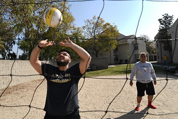 View through a volleyball net of a person about to make contact with a volleyball.